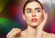 site-industries-cosmetiques A woman with long brown hair and green eyes poses pensively against a colorful background of automobile drafts. She touches her face with one hand, revealing pink lips and pale skin, while the lighting accentuates her features.